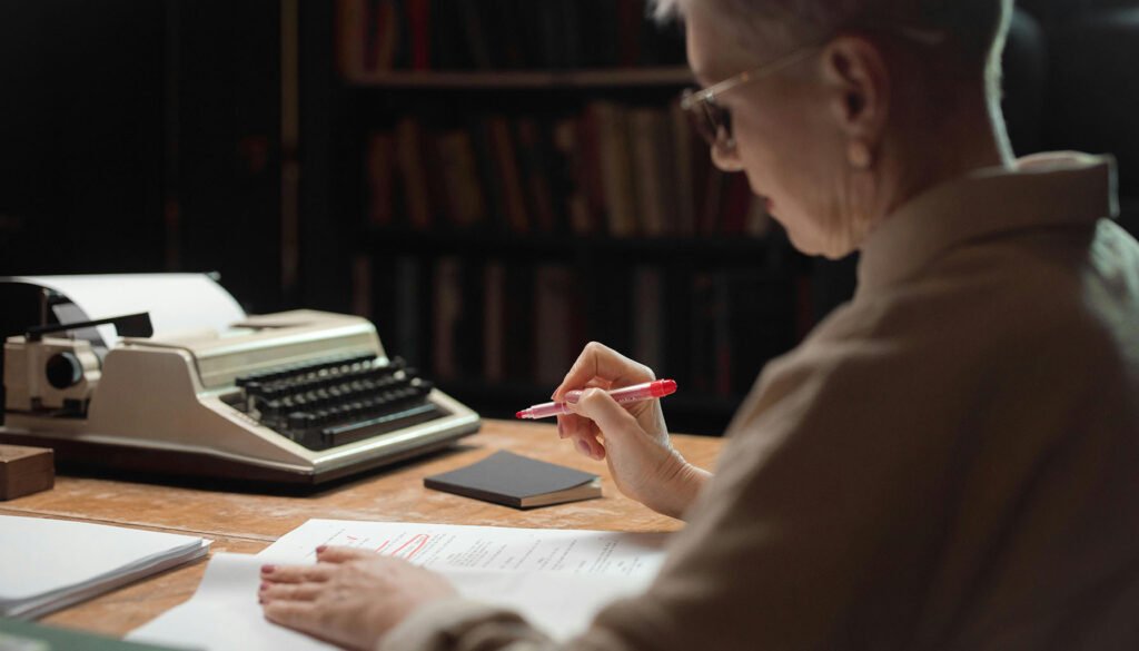 Author carefully reviewing manuscript with professional editing marks and multiple drafts spread across desk